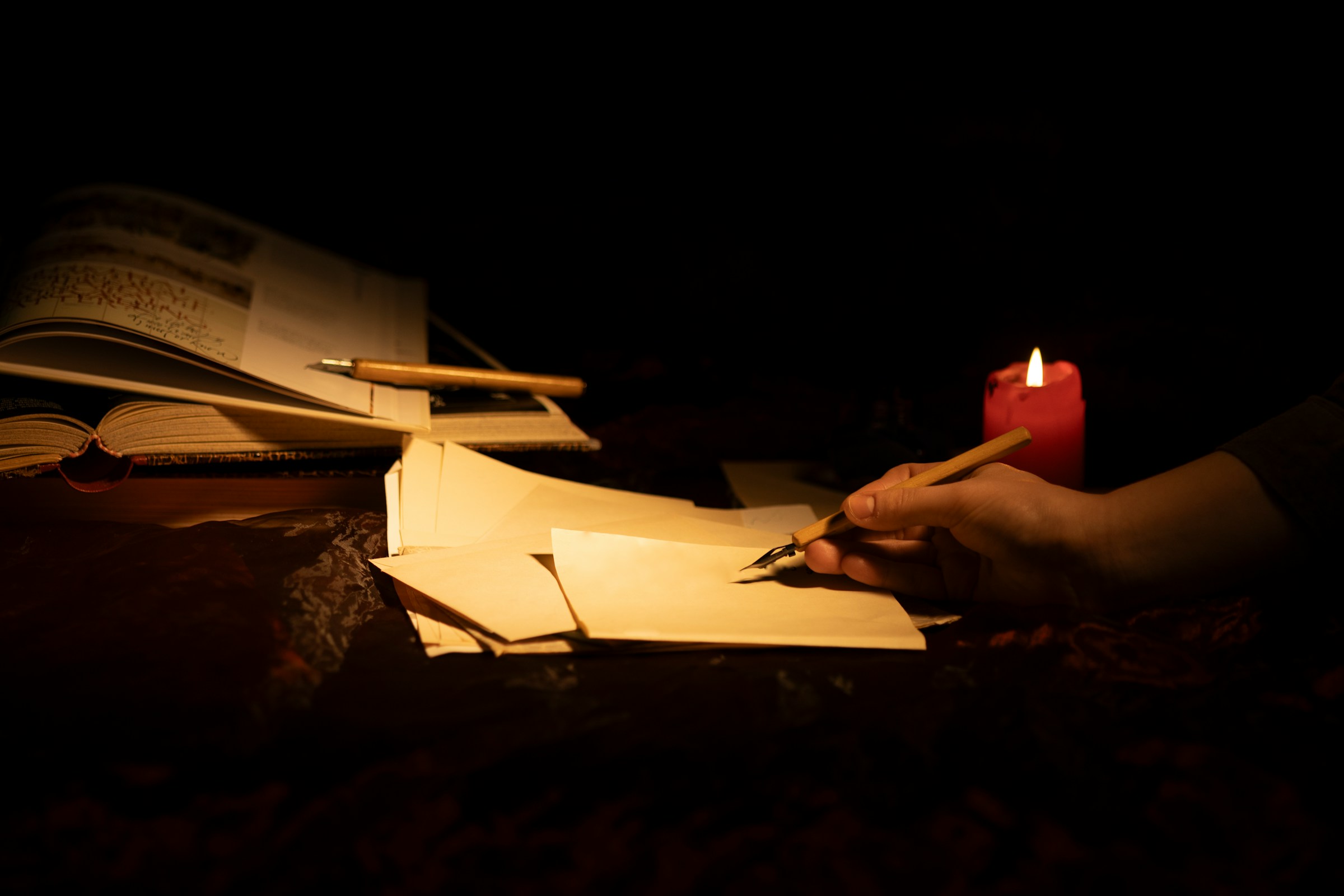 Persona che scrive a mano su un foglio illuminato dalla luce calda di una candela, simbolo del lavoro accurato di un editor professionista di romanzi.